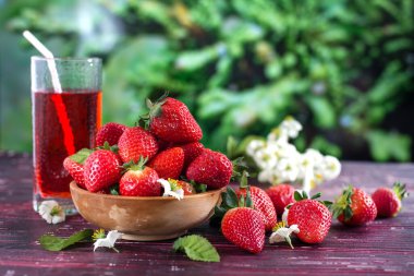 Tahta bir fincanda olgun çilekler bahçede bir masada ve bir bardak çilek suyu