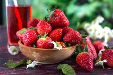 Tahta bir fincanda olgun çilekler bahçede bir masada ve bir bardak çilek suyu