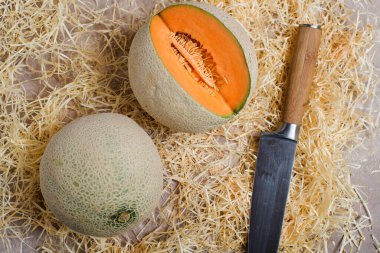 Dilimlenmiş olgun kavunlar ve saman üzerinde bir bıçak. Yukarıdan görünüm