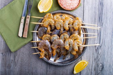 Gümüş tepside karides, gri bir masada peçete, çatal ve bıçakla..