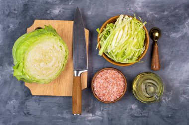 Kesme tahtasında lahana. Tuz, zeytinyağı ve bıçak. Gri arkaplanda üst görünüm