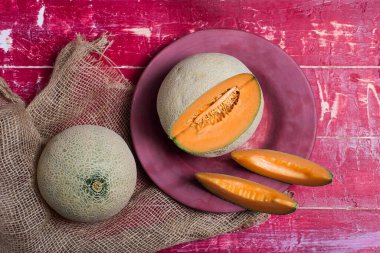 Olgun kavun, kırmızı bir masanın tepesinde bir tabakta dilimler.