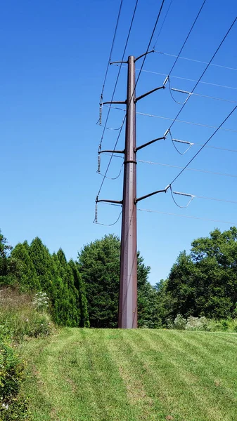 High voltage power lines cross on a large metal pole against a blue sky.