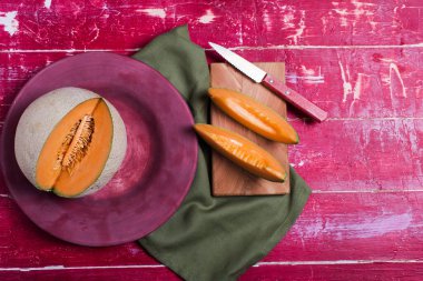 Olgun kavun, kırmızı bir masanın tepesinde bir tabakta dilimler.