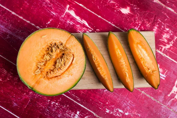 melon with cut slices on a red table on top. on a cutting board
