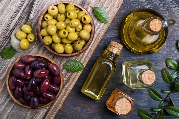 olive oil in bottles and olives in wooden bowls on a textured table top view