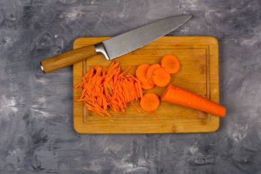 Kesme tahtası manzarasında bıçaklı havuçlar. Gri bir arkaplanda.