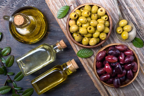 olive oil in bottles and olives in wooden bowls on a textured table top view