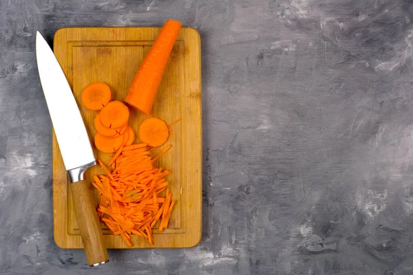 Kesme tahtası manzarasında bıçaklı havuçlar. Gri bir arkaplanda.