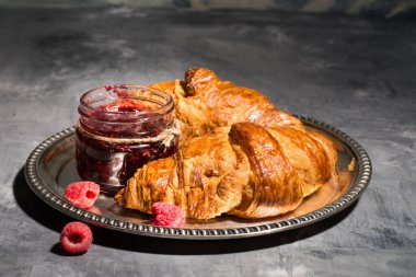 Ahududu reçelli kruvasan ve gri arka planda gümüş tepside ahududu.