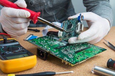Atölyede teknisyen mühendisi. Lehim demiriyle teneke alıyor ve mikro devreye koyuyor. Eldivenli tamirci elektronik cihazın devre kartını lehimliyor..