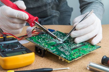 Atölyede teknisyen mühendisi. Lehim demiriyle teneke alıyor ve mikro devreye koyuyor. Eldivenli tamirci elektronik cihazın devre kartını lehimliyor..