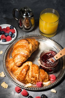 Ahududu reçelli kruvasan ve gri bir masada portakal suyu.