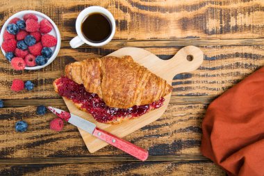 Ahududu reçelli kruvasan ve ahşap bir masada kahve. böğürtlen ve ahududu manzarası