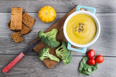 Brokoli püresi çorbası, ekmek kırıntıları ve domatesler gri bir masada. Yukarıdan görüntüle.