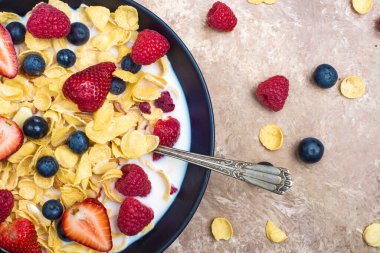 Kahverengi bir masada sütlü mısır gevreği, yabanmersini, çilek ve ahududu. Yukarıdan görünüm.