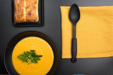 Siyah kasede siyah bir kase sebze püresi çorbası ve siyah masada ciabatta ekmeği..