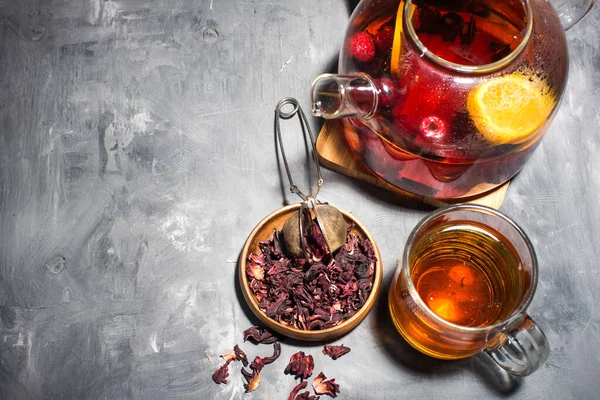 Dry tea leaves, raspberries and tea in a glass teapot. On a gray table. View from above. Space for text.