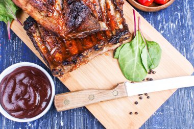 Soslu kızarmış kaburga ve ahşap bir tahtanın üzerinde bıçakla domates.