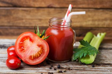 Taze domates suyu bardakta kereviz ve olgun domatesle ahşap masada.