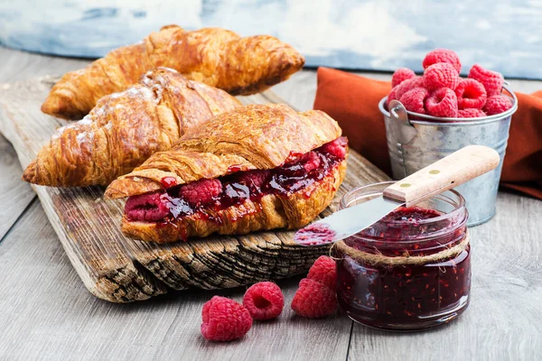 croissant with raspberry jam and raspberries on a textured wooden board. close-up