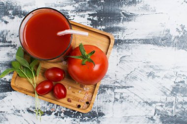 Bardakta taze domates suyu ve gri bir masada olgun domatesler. Kopyalama alanı olan üst görünüm