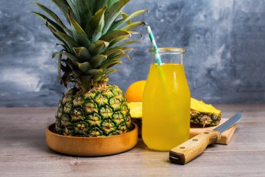 Cam kavanozda taze ananas suyu, gri bir arka planda pipet ve ananas.