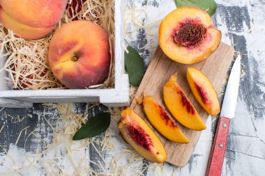 Bıçakla dilimlenmiş şeftali ve masada bir kutu şeftali. Yukarıdan görünüm