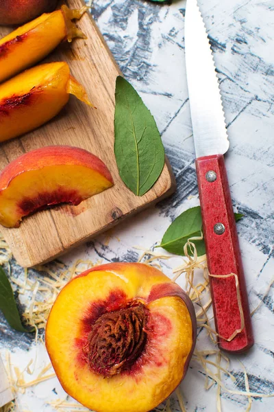 成熟的桃片和一把刀放在灰色桌子上的切菜板上 — 图库照片