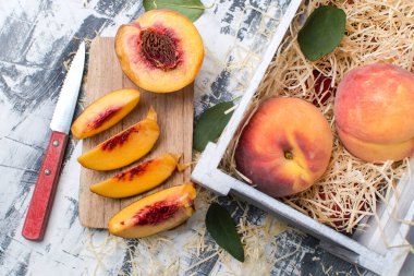 Bıçakla dilimlenmiş şeftali ve masada bir kutu şeftali. Yukarıdan görünüm