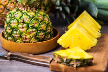 Dilimler ve yarım porsiyon olgun ananas. Tahta kase ve tahta kesme tahtası..