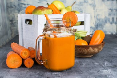 Gri ahşap bir masada şişede taze havuç suyu ve kutuda meyve.