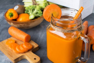 Gri ahşap bir masada şişede taze havuç suyu ve kutuda meyve.