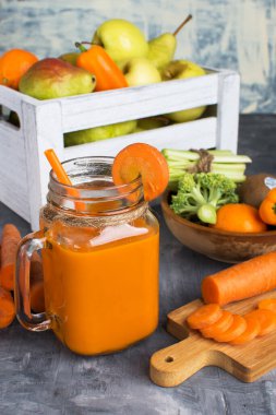 Gri ahşap bir masada şişede taze havuç suyu ve kutuda meyve.