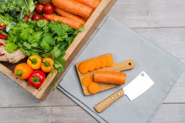 Yüksek açılı natürmort, bıçak ve tahta kesim tahtası, gri masada çiğ sebze çeşitleri.