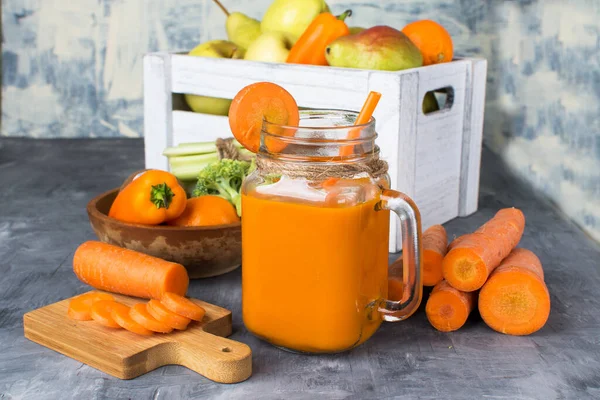 Gri ahşap bir masada şişede taze havuç suyu ve kutuda meyve.