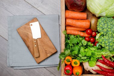 Gri mutfak masasında pişmeye hazır organik sebzeler ve bıçaklı bir kesim tahtası..