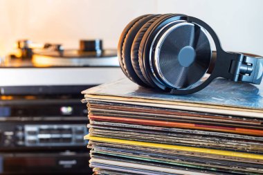 Arka planda modern kulaklıklar ve döner tablolu vinil plaklar yığını