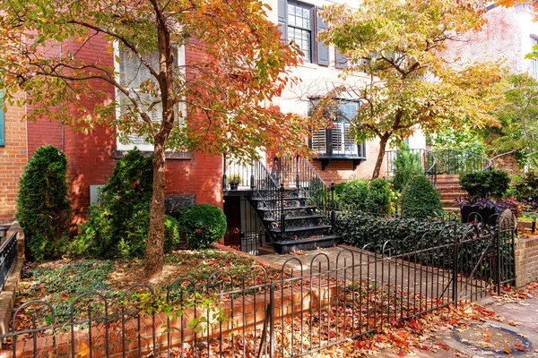 İşlenmiş demir çitler ve sonbahar yapraklarıyla çerçevelenmiş güzel kırmızı tuğla ev. Sonbaharda kentsel cazibenin mükemmel bir temsili..