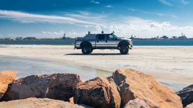 Ufukta savaş gemileri olan kumlu bir sahilde park etmiş gümüş bir kamyonet..