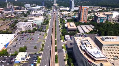 Şehir binaları ve yeşil banliyölerle çevrili otoyol ve metro istasyonunun insansız hava aracı videosu.