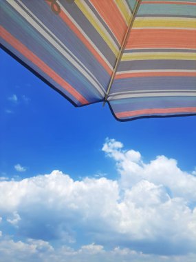 Mavi ve turuncu çizgili şemsiyenin mükemmel bir tatil gökyüzüne karşı detaylarını ve dokusunu gösteren güzel dikey perspektif..