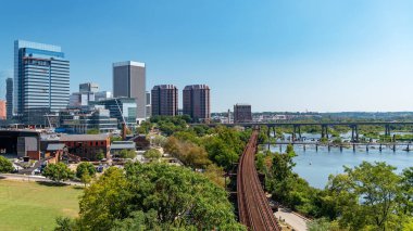 Richmond, Virginia 'nın panoramik manzarasında modern yüksek binalar, James Nehri ve güneşli bir günde tarihi demiryolu rayları yer alıyor..