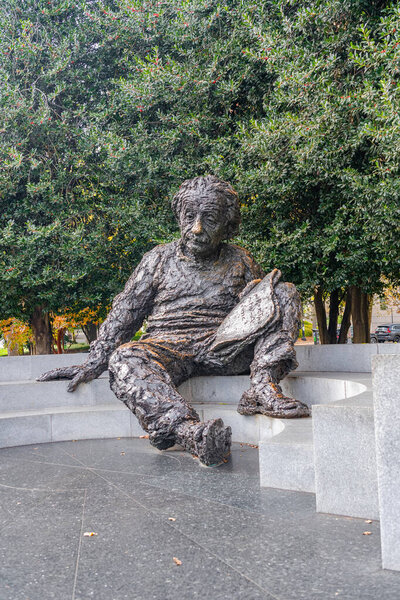 Albert Einstein memorial seated with scientific formulas, surrounded by stone bench and green trees.