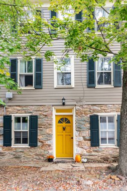 Siyah panjurlu parlak sarı kapı ve taş evin üzerinde şenlikli balkabakları.