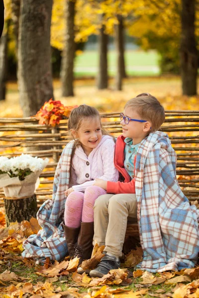两个朋友︰ 一个男孩和一个女孩坐在板凳上的秋园附近的栅栏 — 图库照片