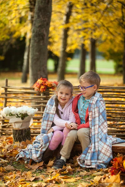 İki arkadaş: bir erkek ve bir kız sonbahar Park ahşap bankta oturan yakınındaki bir çit — Stok fotoğraf