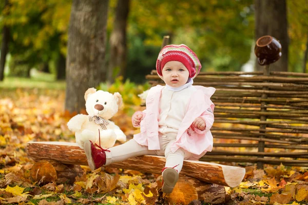 Jong meisje in de herfst park zittend op houten bankje in de buurt van een hek — Stockfoto