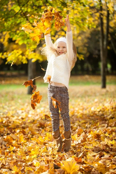 小女孩向树叶扔在秋天的公园 — 图库照片