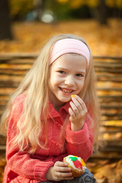 Молодая девушка ест сладкий кекс в осеннем парке — стоковое фото